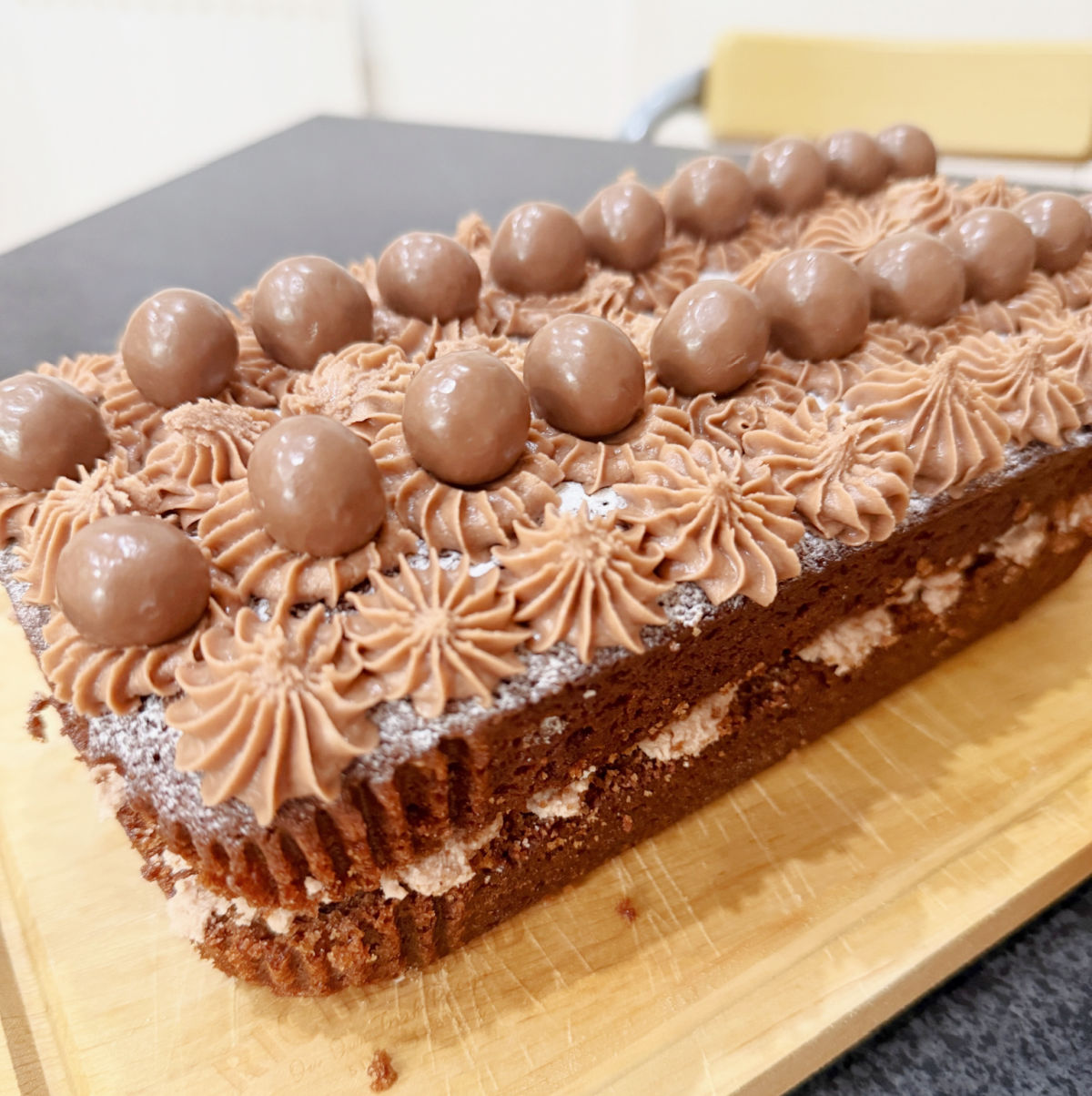 Chocolate Loaf Cake filled and topped with chocolate buttercream and Maltese's on a wooden board